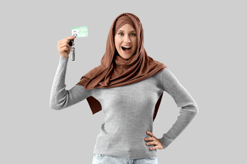 Happy young Muslim woman with driving license on grey background
