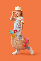 Cute little girl with wicket handbag, headphones and toy windmills on orange background