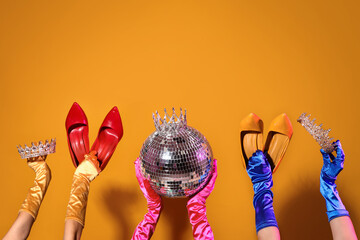 Female hands in gloves with disco ball, tiaras and high heels on orange background © Pixel-Shot