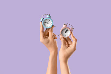 Female hands with alarm clocks on lilac background