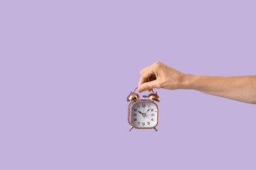 Female hand with alarm clock on lilac background