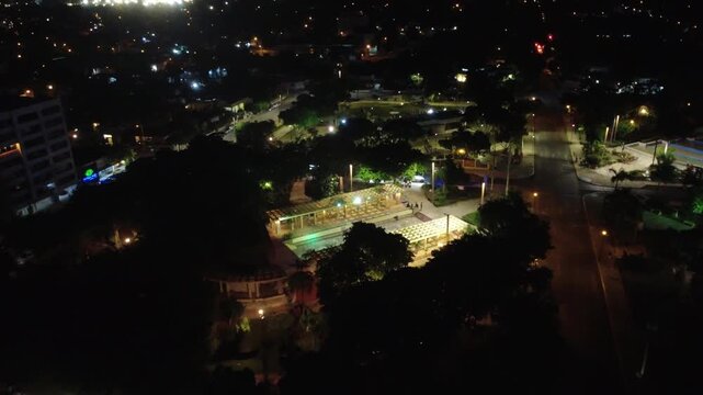 High aerial night shot of Las Am&eacute;ricas park in M&eacute;rida, showing people gathering, warm lighting, and surrounding urban streets. Captured with a 4K UHD drone.