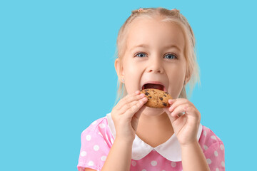 Cute little girl eating tasty cookie on blue background