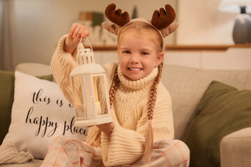 Fototapeta premium Cute little girl with Christmas lantern sitting on sofa at home