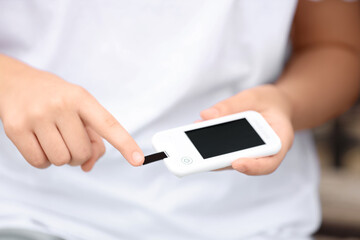 Teenage diabetic girl with digital glucometer taking blood sample on bench in park, closeup