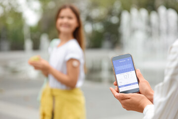 Young woman and her diabetic daughter with continuous glucose monitor using mobile app for sugar level measuring in park