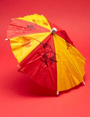 Vibrant Red and Yellow Cocktail Umbrella on a Striking Red Background, Perfect for Summer Drinks and Tropical Themes.