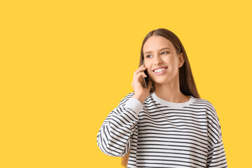 Beautiful young woman talking by modern mobile phone on yellow background
