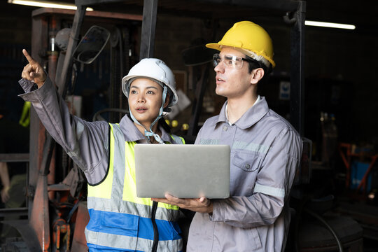 Industrial engineers discuss safety plan inside factory workshop, focused teamwork hard hat, reflective vest, laptop check, machinery background and confident guidance with calm professional mood