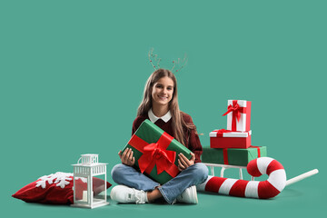 Teenage girl with Christmas gift sitting on green background