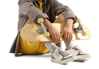 Young man with skateboard sitting on white background