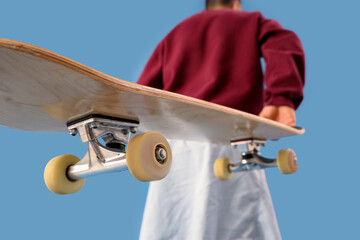 Young man with skateboard on blue background, closeup © Pixel-Shot