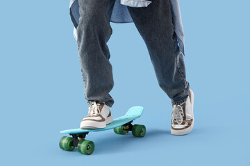 Legs of young man with skateboard on blue background, closeup © Pixel-Shot