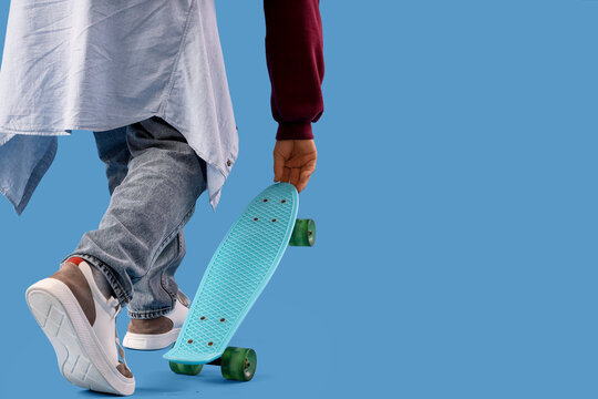 Legs of young man with skateboard on blue background, closeup