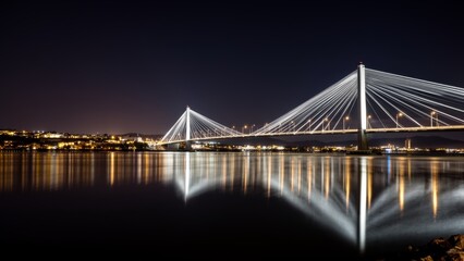 Fototapeta premium Bright lights illuminate the cable-stayed bridge reflecting on calm waters at night