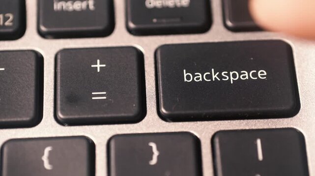 The index finger presses the BACKSPACE key on the laptop keyboard.