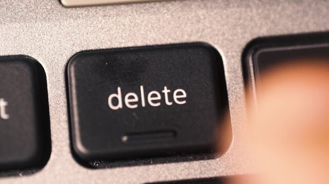 The index finger presses the DELETE key on the laptop keyboard.