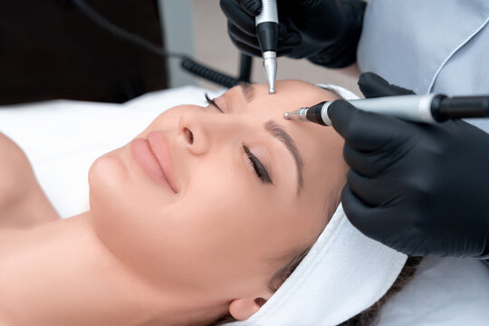 Cosmetology. Beautiful Woman At Spa Clinic Receiving Stimulating Electric Facial Treatment From Therapist. Closeup Of Young Female Face During Microcurrent Therapy