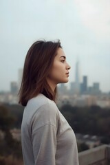 Thoughtful young woman standing outdoors in a soft cityscape background, peaceful mood and calm atmosphere with urban skyline and muted tones