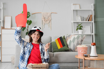 Beautiful young woman with foam finger, pizza and German flag watching match at home