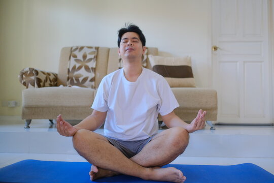 A man is sitting on a blue mat and meditating