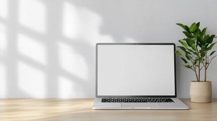 Fototapeta premium Minimal laptop on wooden desk with soft window light and potted plant, calm workspace mood