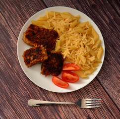 Fried meat cutlets, ripe tomato slices and macaroni sprinkled with cheese on a wooden table.