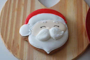 A festive Christmas display with various decorated cookies (Santa, Mrs. Claus, gingerbread man) on wooden boards and a heart-shaped plate, surrounded by holiday decor.