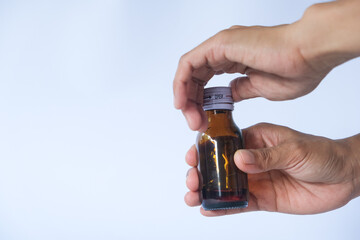 Someone is twisting open the cap of a cough syrup bottle containing bright red liquid.