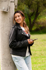 Young woman smiling using smartphone leaning on pole