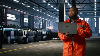 Technician manages operation procedures with handheld laptop, highlighting engineering responsibility and labor strength while he walks around on the factory floor. Workshop fabrication. Camera A.