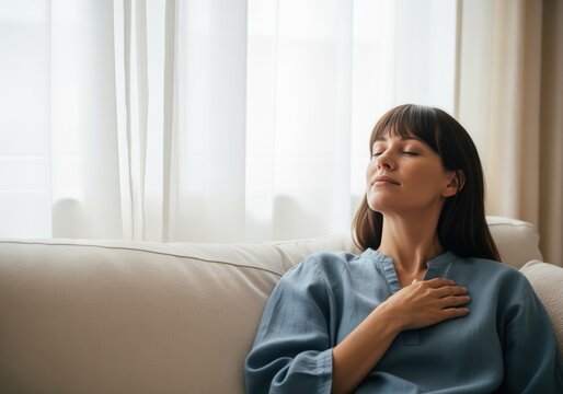 Serene woman meditating on a sofa, eyes closed, experiencing tranquility and peace.