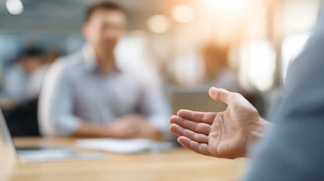 A man in a suit is gesturing with his right hand in a meeting room.