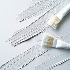 Two white paint brushes and white brushstrokes on a white background, creating a minimalist and abstract composition.
