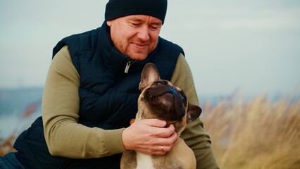 A Joyful Moment Between a Man and His French Bulldog Surrounded by Nature, Capturing the Essence of Companionship and Happiness in the Calm Outdoors