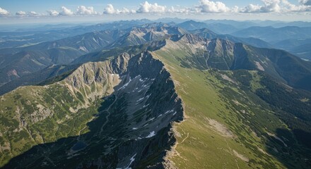 Sweeping aerial view of rugged mountain range, lush green slopes, and distant peaks under a clear sky