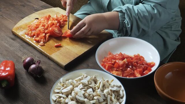 A woman's hands slice red tomatoes with a knife on a cutting board on the table