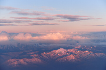 Pink Caucasus mountains with snow peaks in aerial winter scene at sunset. Aerial view from plane.