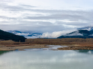 Tranquil Mountain River Scene in British Columbia, Canada With Snowy Peaks and Misty Clouds
