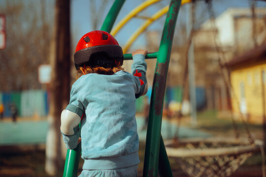 Child with Protective Equipment Climbs at the Playground. Overprotective parenting style concept image of a kid wearing safety gear
