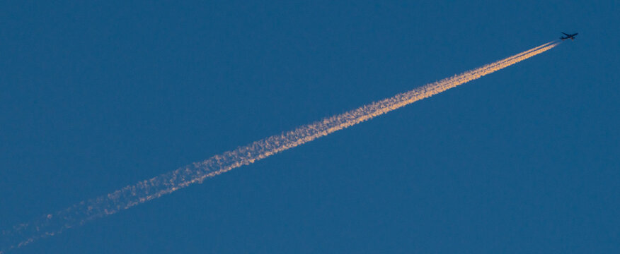 A jet streaking across a deep blue sky trailing pink contrails
