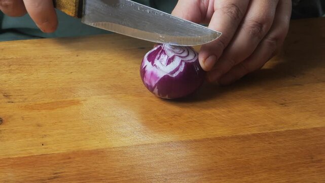A woman's hands slice a red onion with a knife on a cutting board on the table