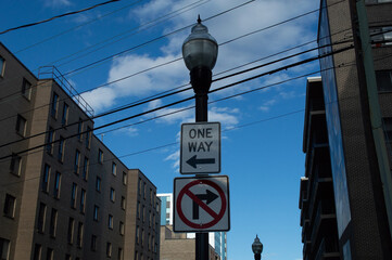Black Lamppost with "One Way" Arrow and "No Right Turn" Traffic Signs Against a Blue Sky and Urban Brick Buildings.