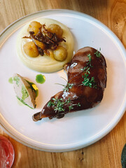 Gourmet dish featuring roasted duck leg with creamy puree and crispy potatoes on a wooden table