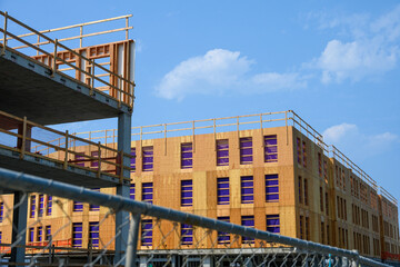 New multistory commercial construction project, wood, sunny summer blue sky day wood framing with plywood exterior walls with purple cloth protective covering in windows
