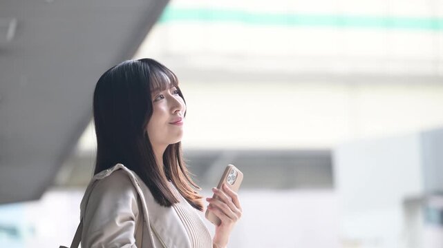 空港や交通機関のターミナルででスマホを持つ女性の写真　旅行や休日のイメージ横顔の動画　笑顔で見上げる