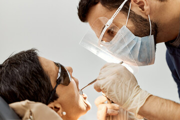 Middle aged Caucasian woman reclining in dental chair receiving oral examination from young adult...