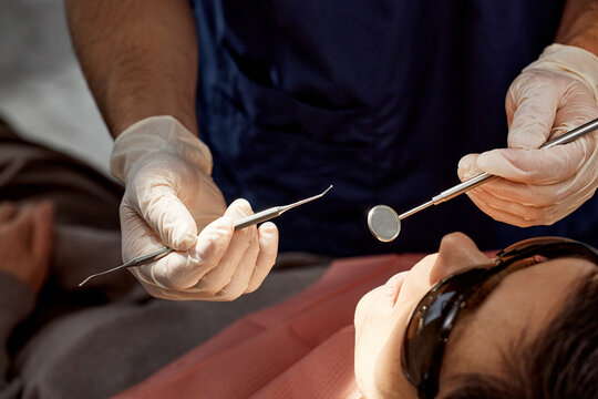 Caucasian woman reclining in dental chair receiving examination from male dentist wearing gloves, dentist holding dental mirror and explorer near patients mouth