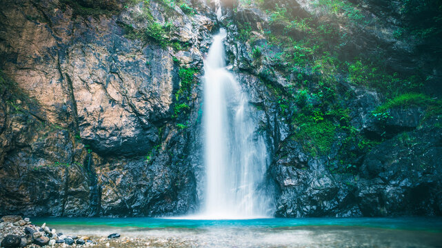 Majestic waterfall cascading over rocky cliffs into a turquoise pool in the forest. - Powered by Adobe