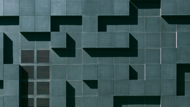 Modern architectural facade with dark green geometric tiles and ventilation grates.